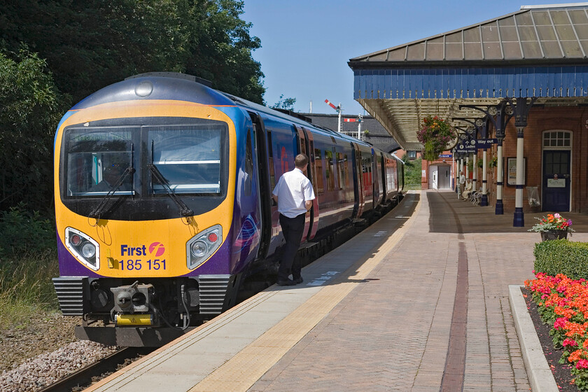 185151, TP 10.29 Manchester Airport-Blackpool North, Poulton-le-Fylde station 
 The guard of the 10.29 Manchester Airport to Blackpool TPE service peers along the length of the train ready to give the driver the RA from Poulton-le-Fylde with the down home signal already pulled off. Notice the huge border of geraniums to the right and the super display of hanging baskets under the awning. 185151 has just about ten minutes to go and no further scheduled stops before arriving at its destination. 
 Keywords: 185151 10.29 Manchester Airport-Blackpool North Poulton-le-Fylde station TE Trans Pennine Express