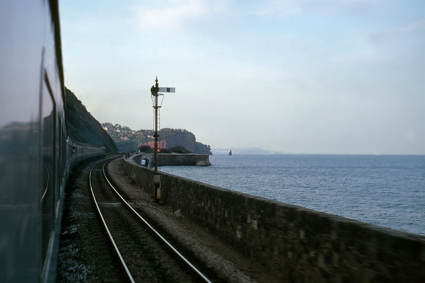 From 16.23 Penzance-London Paddington, Teignmouth sea wall 
 Oh, for the glory of droplights! About to pass the Teignmouth down-home, the South Devon sea wall is seen looking forward towards Sprey Point. Whilst the train and immediate foreground is in deep shadow with the sun having set it is still just managing to catch the Permian red sandstone above Parson's tunnel in the distance. The evening promenaders will be enjoying the English Electric soundtrack of 50027 'Lion' leading our train, the 16.23 Penzance to Paddington substituting for an HST. My travelling companion and technical drawing teacher, Mr. Brush, is seen leaning from the coach in front, also with his camera poised to take a similar photograph to myself! 
 Keywords: From 16.23 Penzance-London Paddington Teignmouth sea wall