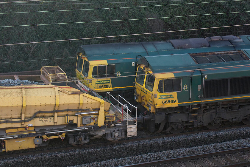 66568, Crewe Basford Hall-Crewe Basford Hall (6Y10) & 66569, Crewe Basford Hall-Crewe Basford Hall return (6Y11), Ashton Road bridge 
 Switched off and idle consecutively numbered 66568 and 66569 sit side by side on the up and down fast lines between Roade and Ashton. Both locomotives were leading infrastructure stock with the fabled 'drain train' being nearest to the camera. 66568 was leading a loaded ballast train. I am not sure as to when they were started up and moved but at least one was still present on the following morning. 
 Keywords: 66568 6Y10 66569 Crewe Basford Hall 6Y11 Ashton Road bridge