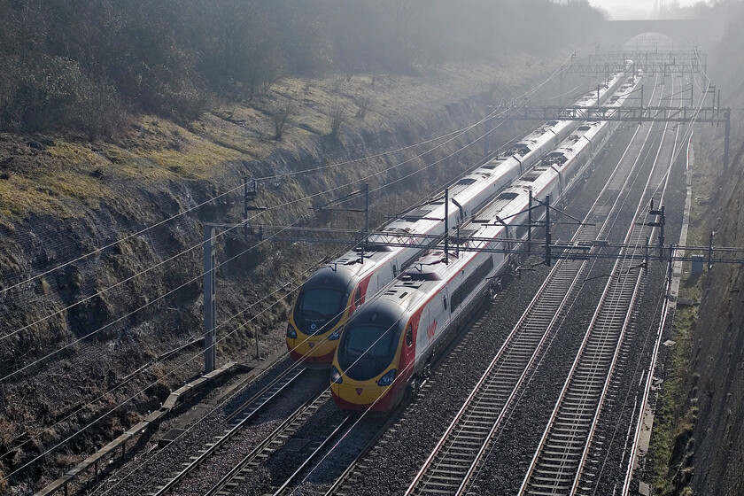 390122, 08.42 Oxley-London Euston ECS (5A16) & Class 390, 10.15 London Euston-Liverpool Lime Street, Roade cutting 
 A passing of Pendolinos in Roade cutting sees 390122 'Penny the Pendolino' head south on the 10.15 Oxley to Euston ECS whilst another member of the class heads north with the 10.15 Euston to Liverpool service. Both locomotives are on the slow lines due to engineering works closing the Weedon route meaning a slow diversion via Northampton. 
 Keywords: 390122, 08.42 Oxley-London Euston ECS 5A16 Class 390 10.15 London Euston-Liverpool Lime Street Roade cutting Penny the Pendolino Virgin Pendolino