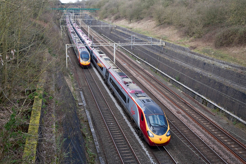 Class 390, VT 12.37 London Euston-Manchester Piccadilly (1H67, RT) & 390001, VT 12.30 Birmingham New Street-London Euston (1B21, 4E), Roade Cutting 
 At a passing speed of somewhere near to 200mph two class 390 Pendolinos cross in Roade Cutting. On the down is the 12.37 Euston to Manchester and on the up is 390001 'Virgin Pioneer' working the 12.30 from New Street to Euston. 
 Keywords: Class 390 1H67 390001 1B21 Roade Cutting