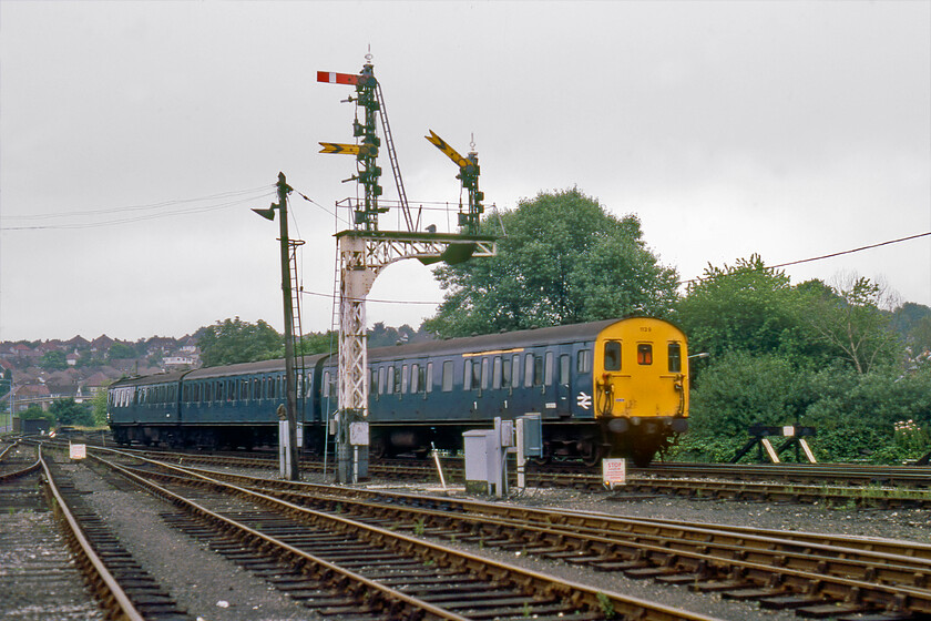 1129, up ECS, Salisbury East Yard 
 A three-car Class 205 trundles away from Salisbury through the East Yard on an unidentified empty stock move. It is passing under the grand up twin doll bracket signal of the traditional Southern Railway latticed design. Both the dolls carry Salisbury Tunnel Junction's distant signal arms one of which is pulled off. I am not sure as to where 1129 was heading but it could well have been the initial departure from Salisbury station's south-facing bay platform before reversing and crossing over to be stabled on the northern side of the station but that begs the question as to why the distant is off? 
 Keywords: 1129 up ECS Salisbury East Yard Class 205 DEMU Thumper