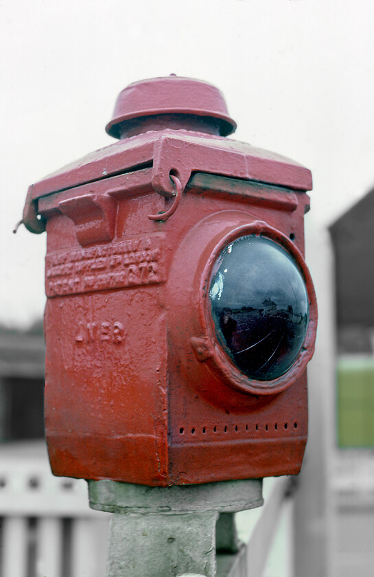 Oil lamp, Habrough level crossing 
 Atop one of the level crossing gates at Habrough a former LNER oil lamp sits continuing to do its job many years after it was installed. This was just one example of many grouping era infrastructures that we observed in this railway backwater of North Lincolnshire. It is only after that I scanned the slide and processed it in Photoshop that I noticed a reflection of a seventeen-year-old me in the globe of the lamp! 
 Keywords: Oil lamp Habrough level crossing LNER