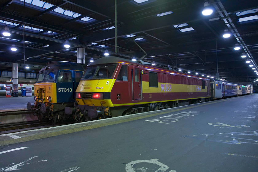 57313, Southall-London Euston ECS (5Z86) & 90039, SR 23.40 Glasgow & Edinburgh-London Euston sleeper (1M11), London Euston station 
 In the darkness and gloom of an early morning inside Euston station, I needed to find something to rest the camera on in order to avoid motion blur from a long exposure of 1/6th second at f5 hence the low angle. At the far eastern side of Euston are platforms one and two. PLatform one is one of two platforms that can accommodate the sleeper services due to their length. 90039 has arrived with the 1M11 Lowland sleeper from Glasgow and Edinburgh that joins in the middle of the night at Carstairs Junction. To the left 57313 with its oversized cabside number has just arrived with the 5Z86 empty stock working from Southall that will be used for The Cumbrian Mountain Express charter. 
 Keywords: 57313 Southall-London Euston ECS 5Z86 90039 23.40 Glasgow & Edinburgh-London Euston sleeper 1M11 London Euston station