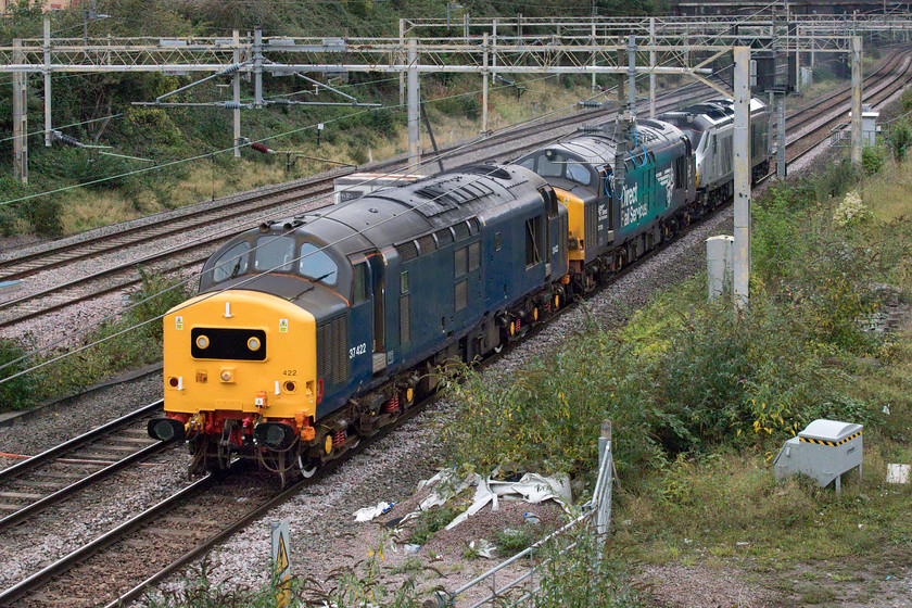 37422, 37038 & 68010, 06.45 Crewe Gresty Bridge-Wembley LMD (0A68), site of Roade station 
 The 0A68 06.45 Crewe Gresty Bridge to Wembley is a regular Saturday morning turn for the return of a DRS Class 68 to Wembley for Chiltern following regular maintenance and an exam. However, today's run was a little different with it being led by two Class 37s that were then going to be continuing onwards to Norwich for RHHT duties. Passing the site of Roade station 37422 leads 37038 with 68010 'Oxford Flyer' at the rear. 
 Keywords: 37422 37038 68010 06.45 Crewe Gresty Bridge-Wembley LMD 0A68 site of Roade station Oxford Flyer