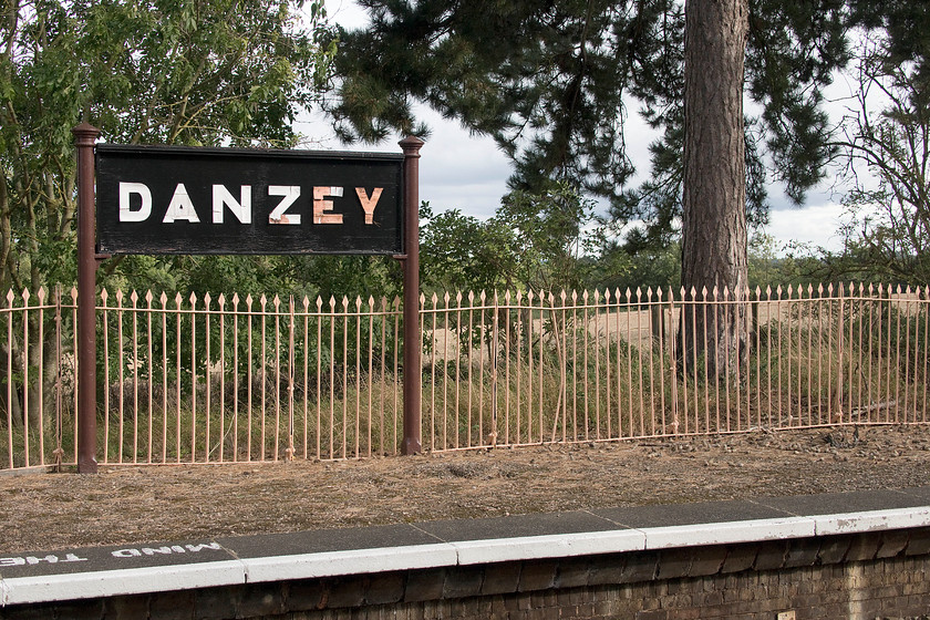 Running-in board, Danzey station 
 A reproduction GWR style running-in board at Danzey station. The station was opened by the GWR in 1908 as Danzey and Tanworth with facilities including a goods yard, a modular station building (down platform) and waiting shelter (up platform). I took this picture to show the original GWR fencing that can be seen in contemporary photographs and the mature Scotts pine trees behind, trees typically planted at many GWR stations. 
 Keywords: Running-in board Danzey station