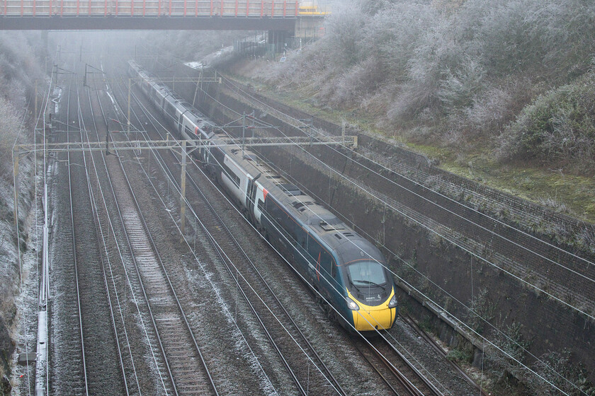 390042, VT 09.35 Liverpool Lime Street-London Euston (1A15, 6L), Roade cutting 
 Passing under the newly constructed bridge that spans Roade's historic cutting that will carry the village's long-awaited bypass 390042 emerges from the cold fog on the Northampton slow line. The Avanti West Coast 09.35 Liverpool to Euston train is one of the new and improved services as part of the roll-out of the company's new timetable following a turgid time on the WCML for some months that found the government getting involved and the imposition of an improvement plan back at the start of the autumn. 
 Keywords: 390042 09.35 Liverpool Lime Street-London Euston 1A15 Roade cutting