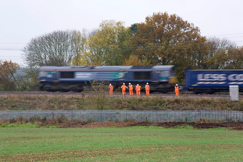 66302, 11.00 DIRFT-Purfleet (4L48), track workers on up & down slow lines between Roade & Ashton 
 The Tesco Express (as it is dubbed) lives up to its name as it heads south between Roade and Ashton on this damp and misty Sunday lunchtime. Due to the trackwork, evidenced in this photograph, the regular 4L48 11.00 ex DIRFT has had to take the fast line south from Rugby to where it headed first before 66302 ran round. This DRS service completes this rather odd avoidance route on a number of occasions throughout the year with the up (or down) slow lines anywhere between Daventry and Hanslope Junction out of use for maintenance. 
 Keywords: 66302 11.00 DIRFT-Purfleet 4L48 track workers on up & down slow lines between Roade & Ashton DRS Direct Rail Services Tesco Express