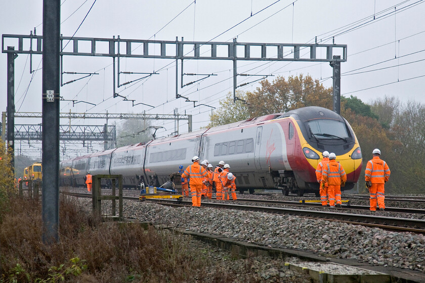 Class 390, VT 11.47 Manchester Piccadilly-London Euston (1B18), track workers on up & down slow lines, Ashton Road bridge 
 A Virgin Pendolino heads south on the fast line between Roade and Ashton working the 11.47 Manchester to Euston service. It is streeking past a number of orange-clad track workers undertaking some ballasting work to the up and down slow lines. It may be a dull day in November but the work on the railways still goes on along with a lot of trains on this very busy section of track. 
 Keywords: Class 390 11.47 Manchester Piccadilly-London Euston 1B18 track workers on up & down slow lines Ashton Road bridge Virgin Pendolino