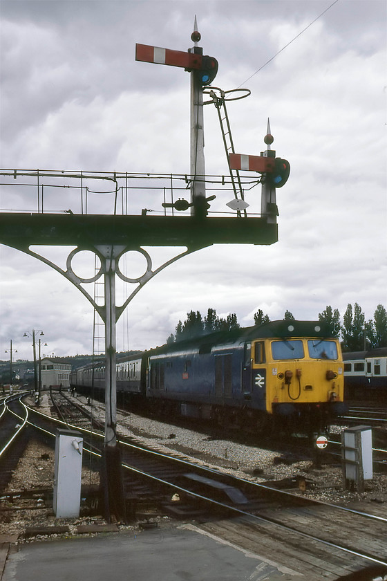 Class 50, unidentified working, Newton Abbot station 
 A photograph that I can provide little information about! I have no record of the Class 50 or the working. This is unusual as I was pretty fastidious even as a sixteen year old about my railway record keeping! All I do know is that it is a picture recovered from the rejects' box and given a fair bit of Photoshop treatment to get it up to a presentable standard. The 50 is entering the station on the down main (the former platform two) passing the up home gantry controlled by the rarely photographed East signal box that is seen in the background. Notice that the dolls on the gantry are wooden, probably dating from proper Great Western days as the later British Railways' replacement versions were grey steel. After nursing the Mini as far as Newton Abbot and dropping off David for his return journey to Bradford-on-Avon by train, Graham and I continued on alone, keeping a very close eye on the car's temperature gauge! 
 Keywords: Class 50 unidentified working Newton Abbot station