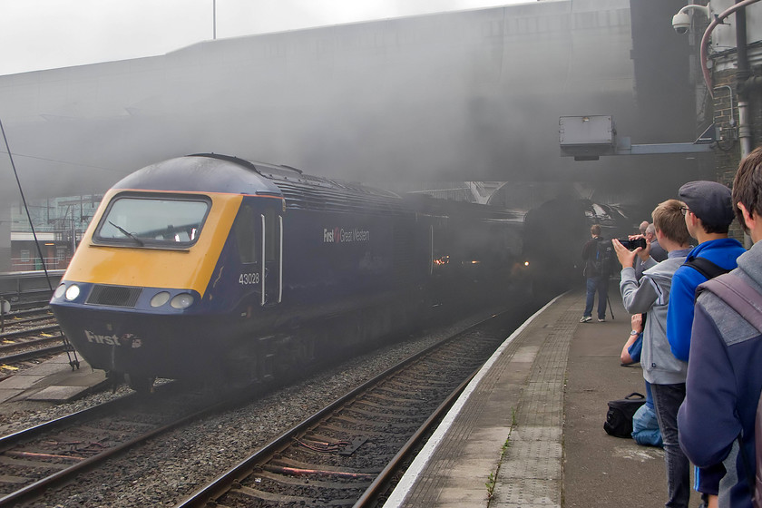 43028, GW 08.00 London Paddington-Bath Spa (1U05) & 70000, outward leg of The West Somerset Steam Express, 08.06 London Paddington-Minehead West Somerset Railway (1Z70), London Paddington station 
 No, this is not a summer fog at Paddington but excess smoke and steam being emitted from 70000 'Britania' hiding under the bridge! To its left, the 08.00 Paddington to Bath Spa HST service leaves led by 43028 no doubt eager to get away from the pollution emitted by the Brit. that will lead The West Somerset Steam Express charter to Minehead. It is really pleasing to note in this image the age of the enthusiasts on the platform end. Yes, there were the usual old blokes like me but note the line of young lads all eager to get their photographs and get them uploaded straight to the internet no doubt! 
 Keywords: 43028 08.00 London Paddington-Bath Spa 1U05 70000 Britania The West Somerset Steam Express 08.06 London Paddington-Minehead West Somerset Railway 1Z70 London Paddington station