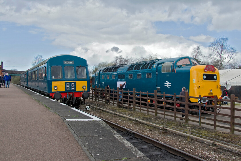 E50266 & E50203, 12.50 Loughborough GCR-Leicester North & 55009, on display, Quorn & Woodhouse station 
 As one of the GCR's resident Class 101 DMUs leaves Quorn and Woodhouse station working the 12.50 Loughborough (GCR) to Leicester North service 55009 'Alycidon' sits on display in the station yard. Notice the avid enthusiast attempting a rubbing of the nameplate, something that many of us youngsters did on the platform ends back in the day! Hopefully reliving his youth the DPS member had come equipped with a tube attached to his rucksack containing a pre-measured and cut length of lining paper, a crayon of some description and some masking tape. Unfortunately, the blustery wind caused him some problems and a fellow enthusiast is just joining him to save the day by helping to attach the flailing lining paper! Of course, his rubbing will not be reading 'Alycidon' as 55009 is seen renumbered and named as 55013 'The Black Watch'. 
 Keywords: E50266 E50203 12.50 Loughborough GCR-Leicester North 55009 Alycidon 550103 The Black Watch Class 101 first generation DMU Quorn & Woodhouse station