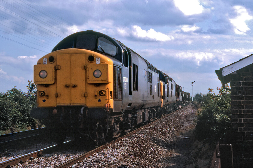 37090 & 37245, down freight, Badgenny Road level crossing 
 Making our way to Horsemoor just south of March we called in at Badgenny Road level crossing. As we were there the gates closed and the crossing's home signal, seen in the middle distance, was pulled off. Being a Sunday in the Fens there was little scheduled passenger traffic so we were pleased to see a freight approaching from the Ely direction probably heading to Whitemoor Yard. 37090 and 37245 lead a short engineering train no doubt shattering the Fenland peace and quiet on this warm Sunday afternoon. 
 Keywords: 37090 37245 down freight Badgenny Road level crossing