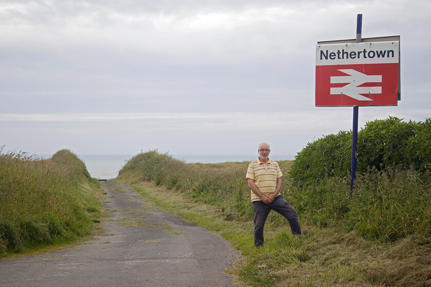 Andy, station sign, Nethertown 
 Andy poses by the station sign at Nethertown on the Cumbrian Coast. The narrow road that soon becomes an un-made track leads steeply down to the station. Surely one of the most dramatic UK stations? Notice the BR double arrow logo that appears to be of a larger font than normal being a little thick or is it my imagination? 
 Keywords: Andy, station sign Nethertown