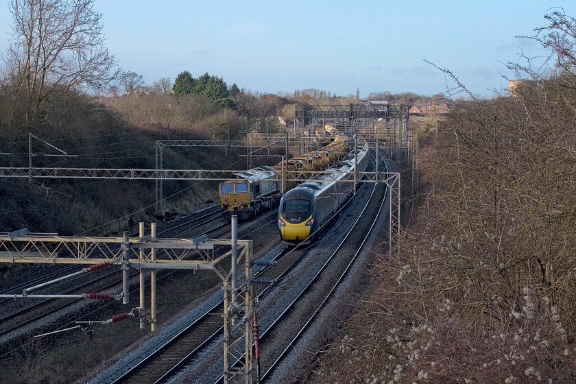 66506, Crewe Basford Hall-Crewe Basford Hall return (6Y11) & 390002, VT 13.18 London Euston-Preston (9P77, 31L), Victoria bridge 
 Whilst 390002 'Stephen Sutton' heads north on the slow line at a very slow speed working the 9P77 13.18 Euston to Preston Avanti service 66506 is seen idle at the rear of an infrastructure train. This is the final Class 66 seen and photographically recorded during this particular Sunday afternoon foray. The Pendolino was the second of a procession of down services running signal to signal at a walking pace. In fact, they were probably in view of each other on the longer and straighter sections of the track behind where I am standing. The picture is taken from one of my favourite local spots, Victoria bridge that I have recently learnt was also known as Coronation bridge in earlier times. 
 Keywords: 66506 Crewe Basford Hall 6Y11 390002 13.18 London Euston-Preston 9P77 Victoria bridge 	Stephen Sutton