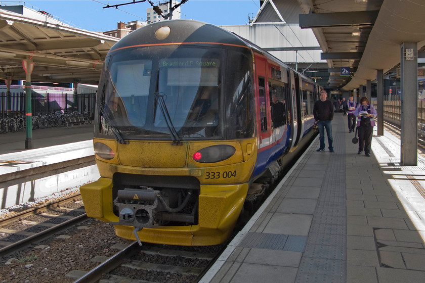 333004, 11.40 Leeds-Bradford Forster Square (2P40), Leeds station 
 With the exception of the gaping hole accommodating the coupling mechanism, I think that the front-end design of the class 333s operated by Northern on the Wharfedale and Airedale routes out of Leeds look very smart with their elegant curved screens reminiscent of some first-generation electric and diesel multiple units. Our final train of the journey from Northampton to Bradford waits to leave Leeds as the 11.40 to Forster square. This was my first ride on one of these units despite them be introduced some fifteen years ago. My boss, Trevor, is seen standing next to the train looking excited about his ride too! 
 Keywords: 333004 11.40 Leeds-Bradford Forster Square 2P40 Leeds station Northern Trains West Yorkshire Metro