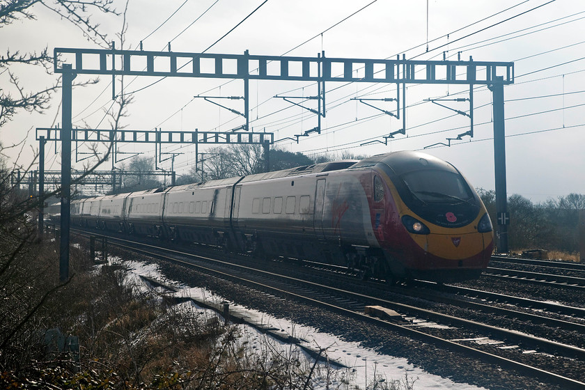 390103, VT 10.20 London Euston-Manchester (1H05 ), Ashton Road bridge 
 As the snow continues to melt rapidly a faint hint of sun emerges from the clouds....is the Beast from the East finally beaten? 390103 'Virgin Hero' passes Ashton Road bridge on the down slow near Roade with the 10.20 London Euston to Manchester Piccadilly. It is quite common for the Weedon line to be closed all night on Saturday and into Sunday morning, with normal service usually resuming by mid-morning. 
 Keywords: 390103 1H05 Ashton Road bridge