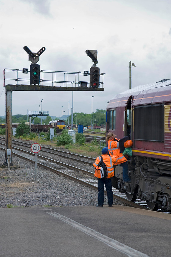 Crew change, 66096, 13.30 Appleford Sidings-Whatley Quarry, Westbury station 
 66096 has come to a halt at Westbury's 102 starter signal for a crew change but the signal has already gone green and the feather illuminated to show that the route is set for GW line to Fairwood Junction. In the modern world, it's encouraging to see that females can do jobs that, in the past, were seen as the preserve of males. 
 Keywords: Crew change 66096 13.30 Appleford Sidings-Whatley Quarry Westbury station EWS DB Schekner