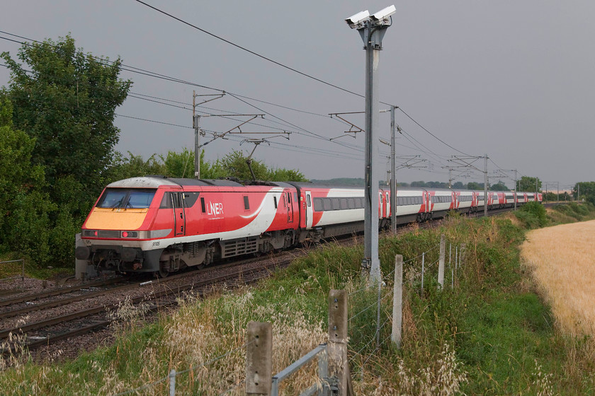 91105, GR 15.30 Edinburgh Waverley-London Kings Cross, started from Newcastle (1E21, 91L), Grove Road Crossing SK717791 
 With the overgrown CCTV cameras looking at Grove level crossing just south of Retford, 91195, wearing its new LNER logo, propels the 15.30 Edinburgh to King's Cross. Despite its advertised start point, this service did not originate from Edinburgh but from Newcastle still managing a 91 minute late arrival into London. This was due to a massive thunder storm that wiped out signalling in the York and Leeds areas earlier in the day that caused absolute chaos. As can be seen in this picture, the weather was looking a touch dramatic here in Nottinghamshire! 
 Keywords: 91105 1E21 Grove Road Crossing SK717791