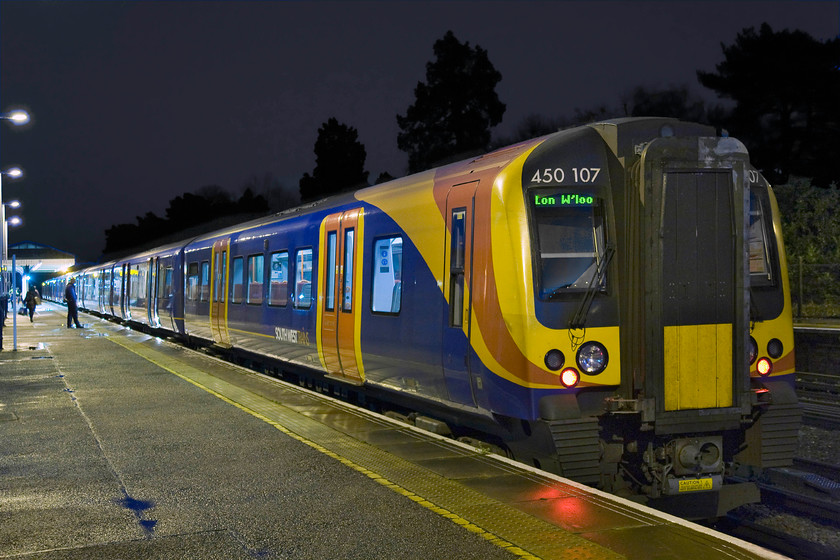 450107, SW 16.15 Alton-London Waterloo (1A54), Brookwood station 
 In the darkness at Brookwood station 450107 pauses with the 16.15 Alton to Waterloo 1A54 service. Behind the looming trees in the background is the huge and famous Brookwood cemetery that is the final resting place of many notable people. A railway was constructed right into both the Nonconformist and Anglican cemeteries by the London Necropolis Railway that brought funeral corteges directly from London Waterloo into two stations withing the cemetery, North (serving the Nonconformist section) and South (serving the Anglican). 
 Keywords: 450107 SWT 16.15 Alton-London Waterloo 1A54 Brookwood station South West Trains