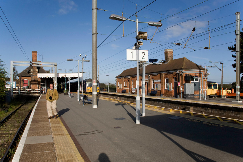 Andy & 360113, 07.58 Harwich Town-London Liverpool Street (1A27), Manningtree station 
 Despite the morning blue sky, it is only the middle of April and it was a bit chilly hence why Andy is sporting his sweater and long trousers with his hands thrust in the pockets! He is seen walking along Manningtree's bay platform one that serves the shuttle trains to and from Harwich as 360113 leaves from platform two with the 1A27 07.58 Harwich Town to Liverpool Street train. 
 Keywords: Andy 360113 07.58 Harwich Town-London Liverpool Street 1A27 Manningtree station Abellio Greater Anglia Desiro