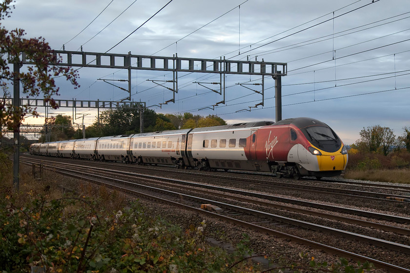 390039, VT 07.23 London Euston-Birmingham New Street (9G05), Ashton Road bridge 
 Virgin's 390039 looks smart in its flying silk livery as it approaches Roade on the WCML working the 07.23 Euston to Birmingham New Street. With the colours in the tress and the foliage, it could only be autumn. The light is also a bit odd due to the after-effects of Storm Callum. 
 Keywords: 390039 VT 07.23 London Euston-Birmingham new Street 9G05 Ashton Road bridge