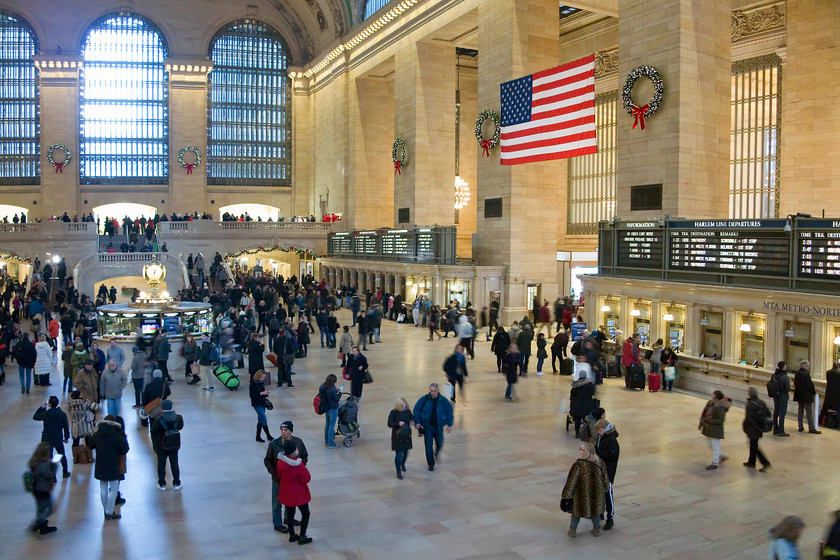 Upper concourse, New York Grand Central station 
 When travellers arrive at Grand Central to travel, they are greeted by this huge and marble clad space. The enormous flag was placed in this spot a few days after the 9/11 attack and has stayed since. Notice my wife and son standing foreground centre right. 
 Keywords: Upper concourse New York Grand Central station