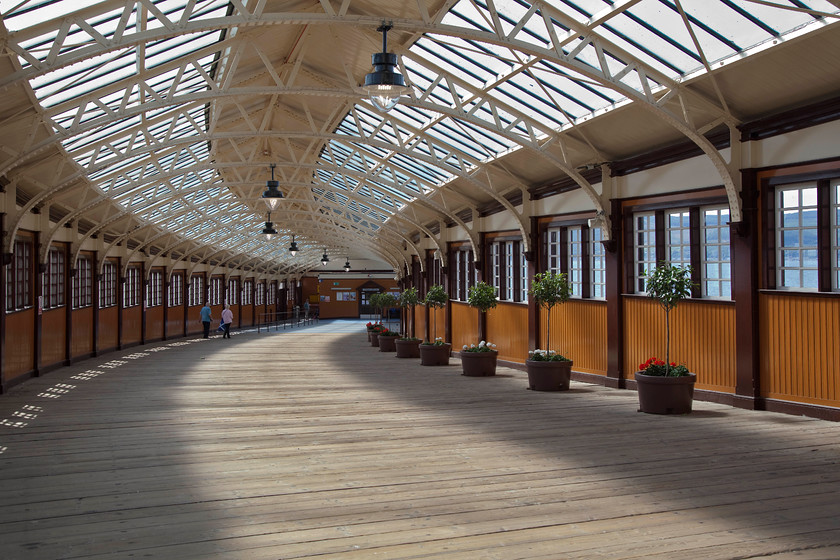 Ramp to ferry terminal, Wemyss Bay station 
 The beautifully restored Wemyss Bay station had a very grand air about it. It underwent a full restoration during 2014. In this image, the concourse is behind me and the view is looking down towards the pier-head where the ferries Rothesay, Largs, Millport, and the Isle of Cumbrae could be taken. Today, the only remaining ferry is to Rothesay, a regular vehicle service that goes from the adjacent ferry terminal. Notice the curved row of bay leaf (laurus nobilis) trees looked after by a dedicated team of volunteer staff who maintain the amazing flora throughout the station. 
 Keywords: Wemyss Bay station