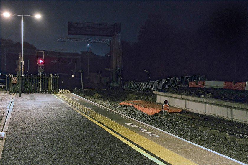 Re-building of platform 4 & relaying of up slow line, Wellingborough station 
 Looking north from Wellingborough station the up and down slow line platforms are seen. Whilst the up platform has been re-built, the track stops abruptly with a stop sign marking where it ends. In the fullness of time, it will be connected to the next section that stops just beyond the new concrete bridge seen in the darkness. Notice the huge signal gantry towering above the line and where the electrification wires will hang. Quite why these structures have to be so over-engineered is beyond me, compare it to the 1980s MAS signal on the platform end! 
 Keywords: Re-building of platform 4 relaying of up slow line Wellingborough station