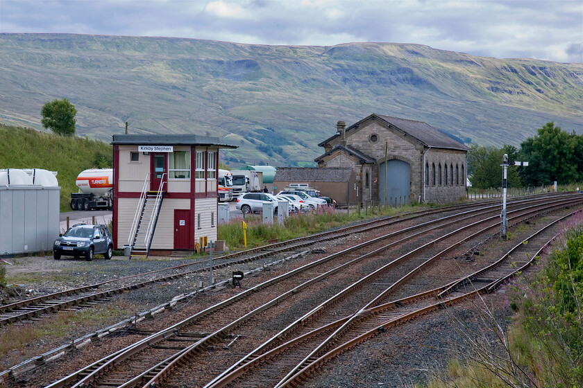 Kirkby Stephen signal box (BR, 1974) & former goods shed 
 The former goods shed at Kirkby Stephen is now in use as commercial premises being occupied by a haulage company. The signal box is a relatively new structure being erected by BR in 1974 making it forty years old this year! The box was formally located at Kendal being moved to its new location a short distance over the fells. I stood in a very similar spot to this back in the spring of 1981 capturing 46229 'Duchess of Hamilton' passing with a northbound Cumbrian Mountain Express, see ..... https://www.ontheupfast.com/p/21936chg/30022686219/x5-46229-outward-leg-cumbrian-mountains. Notice that the down home signal post has been shortened somewhat during the intervening thirty-three years but apart from that little has changed! 
 Keywords: Kirkby Stephen signal box former goods shed