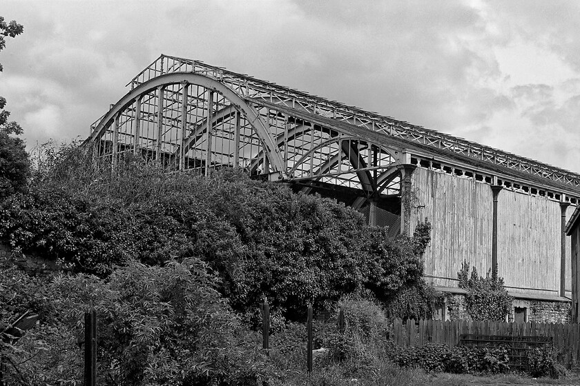 Trainshed, Bath Green Park station, from Midland Bridge Road 
 A slightly wider view of the trainshed od bath's former Green Park station reveals its elegant and symmetrical lines. Looking completely derelict and being slowly overrun by ivy it is surprising that it was only closed some fifteen years previously. However, things were about to change with the site's purchase by the supermarket giant Sainsbury's having been completed and its development about to commence. 
 Keywords: Trainshed Bath Green Park station from Midland Bridge Road