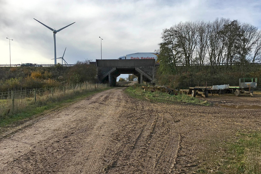 SMJ trackbed, M1 underbridge SP783527 
 A reverse view of the M1 bridge that once crossed the SMJ railway. The wind turbines reveal the location as being next to the M1 wind farm in Northamptonshire. Despite the motorway opening over a year after the railway it crossed here had closed a substantial reinforced concrete bridge was provided! However, in the defence of the planners, the track was still intact and for a few years this section of the line was used to store hundreds pieces of withdrawn stock that must have made quite a sight. 
 Keywords: SMJ trackbed M1 underbridge SP783527