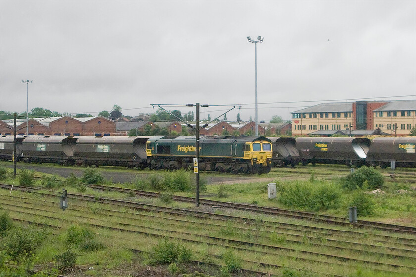 Class 66, 15.26 Drax PS-Tyne coal terminal, York Yard North 
 A pretty poor quality photograph taken as our train enters York from the north. It shows an unidentified Class 66 at the head of a northbound bulk train that has taken the York avoided line and is waiting to rejoin the ECML to continue its journey northwards. However, also of interest is the buildings directly above the train. They are the former NER Holgate Road carriage works that were opened in 1884 but has now been closed. Throughout its working life the works has a proud heritage of railway production but this has been blighted somewhat in recent years with many former workers dying from asbestos-related diseases as a result of the conditions within the plant. 
 Keywords: Class 66 15.26 Drax Power station-Tyne coal terminal, York Yard North