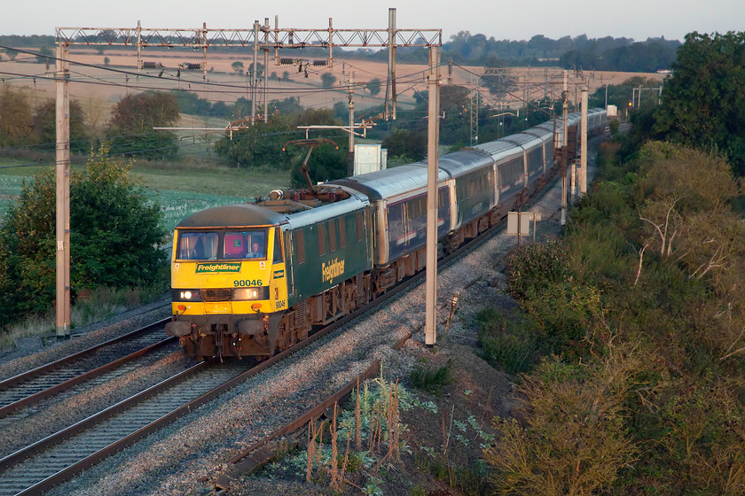 90046, CS 19.50 Fort William, 21.43 Aberdeen & 20.45 Inverness-London Euston (1M16, 3E), Blisworth 
 With the rising sun just above the horizon, 90046 is illuminated leading the Caledonian Sleeper 1M16 Highland service. Today it is running to time following the previous day's disaster with it arriving into Euston a whopping one hundred and eighteen minutes late! The CAF Mk. V stock has still yet to be introduced on the Highland service due to a number of serious technical problems so the Mk. IIIs are still in use but very much but on borrowed time. As this will be the last morning that I will be able to get out and take a photograph near home due to the lack of light, that is unless it is late again, then scenes such as this with the train passing Blisworth will be confined to history. 
 Keywords: 90046 19.50 Fort William 21.43 Aberdeen 20.45 Inverness-London Euston 1M16 Blisworth