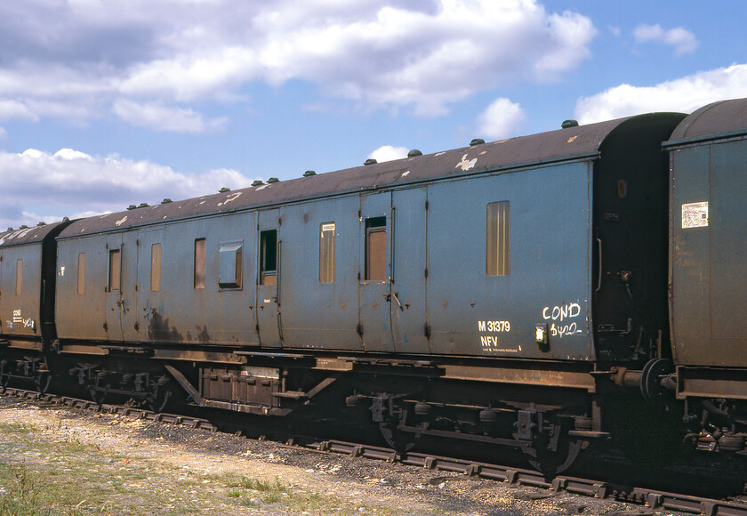 M31379, stored, Whittlesey 
 n some sidings at Whittlesea we came across the extraordinary sight of a huge number of stored stock awaiting its next move and meeting with the scrapman. My records appear to show sixty-three parcel vans on site being a mixture of LMS and Southern types. We spent some time wandering around the sidings not being bothered by anybody and with no security in place; how different to today when redundant stock is only found in secure compounds away from prying eyes and trophy hunters! Former LMS fifty-foot van M31379 stands in line catching the afternoon sun as it awaits onward movement. The sticker in its centre window reads Birmingham. I wonder if this was where it went on its final run with BR before being condemned? 
 Keywords: M31379, stored, Whittlesey