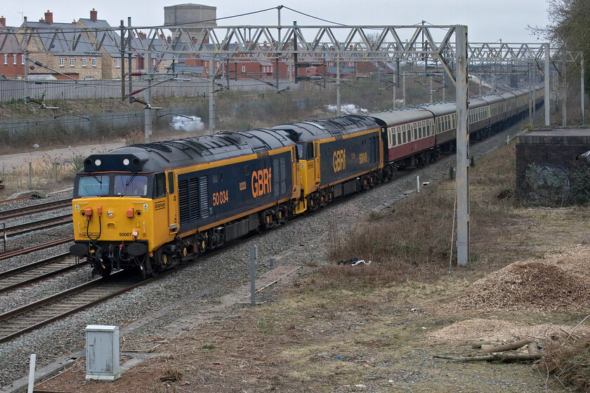 50034 & 50049, 11.27 Wembley Reception sidings-Burton Ot Wetmore sidings (5Z50, 54L), site of Roade station 
 Making an extraordinary row as it passes through Roade the 11.27 Wembley Reception to Burton-Ot-Wetmore empty stock move passes the site of Roade station on the down fast due to the closure of the slow lines for engineering work. Running some hour or so late the train had lost its path so had to be slotted in between other services with the driver no doubt being advised to give it some beans so as not to hold up too many Pendolinos! He appeared to be following the advice and it was really going at some pace catching the attention of some normals who were crossing the footbridge behind me who I had to educate! With a bit of an identity crisis on show, the leading locomotive is not actually 50034 'Furious' as that was scrapped at Old Oak Common in 1991 but is in fact 50007 'Hercules'. 50049 'Defiance' is tucked second inline sharing the same GBRf large logo livery as the leading locomotive but with the addition of a set of mini snowploughs. 
 Keywords: 50034 50049 11.27 Wembley Reception sidings-Burton Ot Wetmore sidings 5Z50 site of Roade station Hoover Furious Defiance Hercules 50007