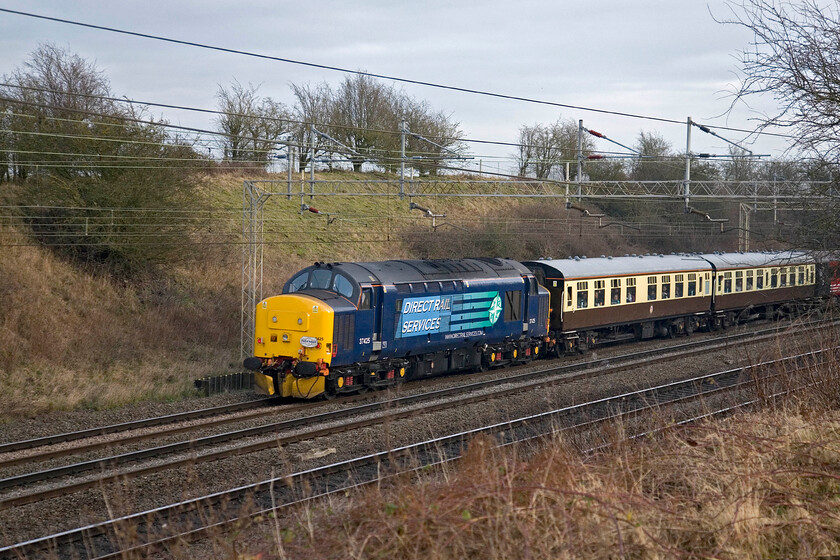 37425, outward leg of The Enigmatic Logistition, 08.21 Crewe-Wolverton (1Z34, 2L), Roade Hill 
 With its engine running but not actually under load 37425 is seen being dragged at the rear of The Enigmatic Logistition charter as it makes its way south between Roade and Ashton. Having missed out on all of its run along the MML to London earlier in the day it is now going to reverse at Milton Keynes and enter the Wolverton Works complex (what's left of it that is) before returning north again after dark. This will mean that the passengers will have covered less than half of their planned itinerary. Incidentally, there was a further long delay encountered later in its journey back through the West Midlands with a passenger taken ill on the train; let's hope that they made a full recovery. 
 Keywords: 37425 The Enigmatic Logistition 08.21 Crewe-Wolverton 1Z34 Roade Hill