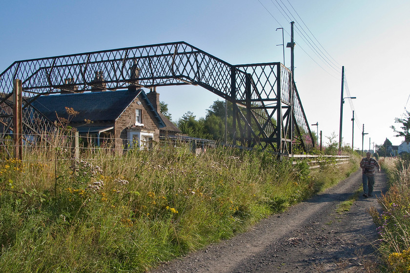 Andy & Errol station (Closed 30.09.85) 
 Andy walks along the track by the side of the now-closed Errol station. The cast-iron footbridge is now somewhat of a skeleton against the brilliant blue summer sky but at least it remains linking together the now very overgrown platforms. Interestingly, on Ordnance Survey maps the small hamlet clustered around the station and the level crossing is named Errol Station with the much larger village of Errol some mile or so to the south close to the Firth of Tay. 
 Keywords: Errol station Closed