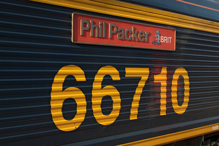 Nameplate, 66710, 15.04 Birch Coppice-London Gateway (4L68, 33L), Rugby station 
 The cast nameplate (unlike some very poor vinyl versions now being applied) on the flank of 66710 'Phil Packer BRIT' as it sits in the evening sun at Rugby station. The 66 leading the 4L68 15.04 Birch Coppice to London Gateway was having a crew change hence its wait at platform six. Phil Packer's story is an interesting and inspirational one that can be read on his website, see.... https://www.philpacker.com/. 
 Keywords: Nameplate 66710, 15.04 Birch Coppice-London Gateway 4L68 Rugby station Phil Packer BRIT