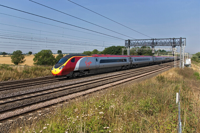 390009, unidentified up working, between Roade & Ashton 
 An extremely wide-angled shot that has needed a fair amount of work in Photoshop to straighten things up to eliminate distortion. 390009 heads south between the villages of Roade and Ashton working an unidentified up Virgin West Coast service. Notice that the wheat fields in the background have recently been harvested an activity that for me induces a feeling of melancholy that the summer is coming to an end. 
 Keywords: 390009 between Roade & Ashton Virgin West Coast Pendolino