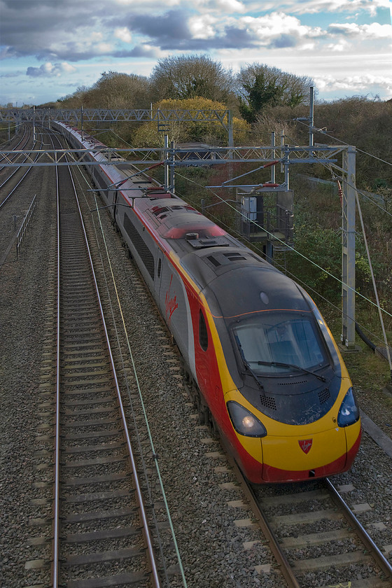 Class 3901XX, VT 14.03 London Euston-Birmingham New Street (9G25), site of Roade station 
 Under a dramatic winter sky, an unidentified Class 390 Pendolino heads north past the site of Roade station forming the 14.03 Euston to Birmingham New Street. Many years ago there was another line to the right of the Class 390 that led to a bay platform behind me. This bay platform and the line was a direct link to the former Stratford-upon-Avon and Midland Junction Railway (SMJR) that crossed the WCML at ninety degrees a short distance south of this location. The short spur never saw much traffic and fell out of regular use early on. 
 Keywords: Class 390 14.03 London Euston-Birmingham New Street9G25 site of Roade station virgin Pendolino