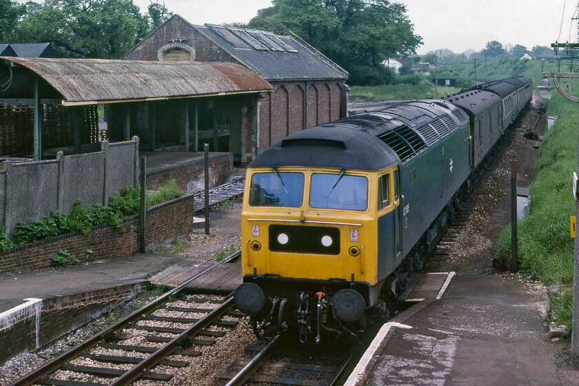 47185, 06.32 Salisbury-Exeter St. David's (2V54), Whimple station 
 47185 leads the 06.32 Salisbury to Exeter St. David's service into the tiny Whimple station. The photograph reveals the superb former Southern Railway good shed that was still in very limited use at this time with transportation of silica stone from nearby quarry evidence of which can be seen with the white dusting on the tracks of the loading bay. There was also an occasional Wagonload service for the village's Whitways Cider company that itself closed in 1989. Unfortunately, the goods shed was demolished in 1990 in an act of absolute vandalism and something that would be unlikely to occur today with the goods yard now occupied by the inevitable housing estate! Notice the various items of prefabricated concrete in this photograph, including the footbridge on which I am standing, all products of the Southern's concrete plant located fairly close at Exmouth Junction. 
 Keywords: 47185 06.32 Salisbury-Exeter St. David's 2V54 Whimple station