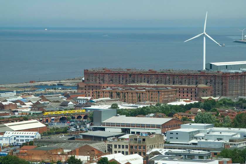 Class 50X, 10.50 Ormskirk-Liverpool Central (2G37), Vauxhall viaduct, from St. John`s Beacon 
 With the expanse of the River Mersey as it enters the Irish Sea in the background, a part of the Port of Liverpool is seen in this view taken from the top of St. John's Beacon Tower, the home to Radio City 96.7. Standing out is a Merseyrail class 50X unit crossing Vauxhall viaduct working the 10.50 Ormskirk to Liverpool Central service. The huge building in front of the wind turbine is the Stanley Dock Tobacco warehouse built in 1901. It is a grade II listed building and is the world's largest brick warehouse. In recent decades it has fallen out of use with calls, notably from the Liverpool Echo, to restore it to use again. There are now plans for it to be converted into the inevitable apartments accompanied by businesses, cafs and retail outlets on the ground floor 
 Keywords: Class 50X 10.50 Ormskirk-Liverpool Central 2G37 Vauxhall viaduct from St. John`s Beacon Mersey