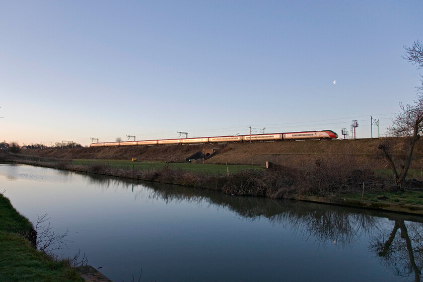 Class 390, VT 06.35 Manchester Piccadilly-London Euston, Whilton Locks SP619640 
 Just catching some early morning sun as it rises above the eastern horizon an unidentified Class 390 Pendolino passes southwards along the side of the Grand Union Canal near Whilton in Northamptonshire. Above the leading power car of the 06.35 Manchester to Euston service the moon in its third quarter phase can be seen. 
 Keywords: Class 390 06.35 Manchester Piccadilly-London Euston Whilton Locks SP619640 Virgin Pendolino