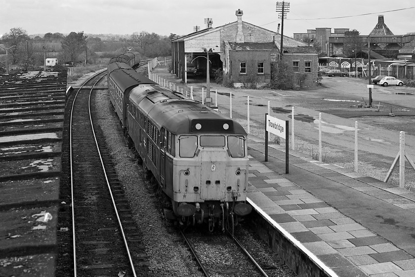 Class 31, unidentified Portsmouth Harbour working, Trowbridge station 
 As it is a Sunday the station car park at Trowbridge station is almost empty. The car park occupies the site of the former and fairly expansive yard with the rather attractive goods shed located in the centre. The goods yard had sidings that served the Bowyers meat factory that can be seen in the background. This was, along with the Ushers brewery and Unigate Dairies one of the three largest employers in Wiltshire's county town at this time. Indeed, my girlfriend's dad worked at Bowyers and my dad for Unigate! In this scene, and unidentified Class 31 passes through the station with an unidentified service probably heading for Portsmouth Harbour. The lovely station buildings were demolished in 1984 and 'modern' monstrosity was built with the main station building moved to the down platform. 
 Keywords: Class 31 Portsmouth Harbour working, Trowbridge station