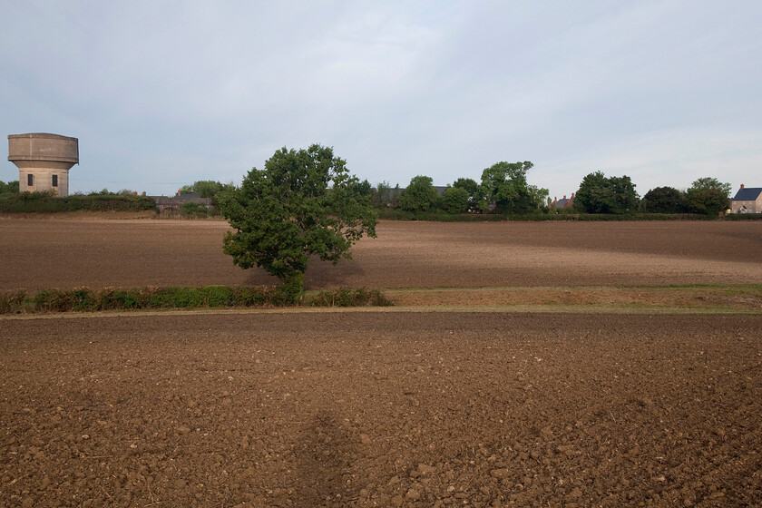 Route of former SMJR, Roade 
 I have taken a similar image to this before but with the field that actually fronts my house off to the right having just been treated to a light tilling (rather than a full-blown plough) by the farmer two days previously the lighter-coloured soil again reveals the route of the former SMJR (Stratford-upon-Avon and Midland Junction Railway) that once passed this location on an embankment and after emerging from the partly hidden road bridge to the left adjacent to the water tower. The eagle-eyed will have spotted that the road bridge that carries Ashton Road is a twin portal version but interestingly, the SMJR was only ever single track at this location leading to its junction with the Midland Railway's Bedford to Northampton (via Olney) route that it joined at the very remotely located Ravenstone Wood Junction. Notice the weak shadow of myself in the centre foreground! 
 Keywords: Route of former SMJR Roade