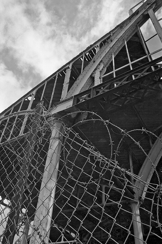 Trainshed & barbed wire, Bath Green Park station 
 Detailing of the leading wrought iron one pice arch that sits on a substantial but nicely detailed pillar at bath Green Park station. Notice the date applied to the structure of 12/57 indicating when the station was last painted. Despite the barbed wire and fencing, it was easy for me to gain access to the station to explore its eerie depths further ignoring the 'Do Not Enter' and 'Danger' signs of course! 
 Keywords: Trainshed barbed wire Bath Green Park station