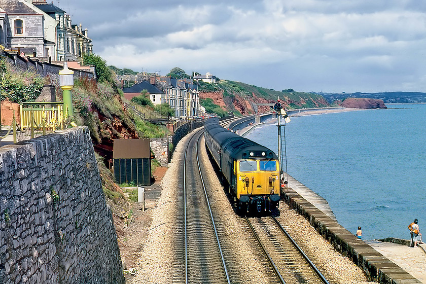 50043, 12.23 London Paddington-Penzance (1B74), Dawlish 
 Memories of long and hot summer holidays! 50043 'Eagle' passes Dawlish on the 1B74 12.23 Paddington to Penzance working. This classic location shows clearly the site of the February 2014 sea wall collapse. The most badly damaged area affected the properties in the mid-distance just beyond the rear coach of the train on Sea Lawn Terrace. This is also the point where the infamous photographs of the track swinging in mid-air were taken. 
 Keywords: 50043 12.23 London Paddington-Penzance 1B74 Dawlish