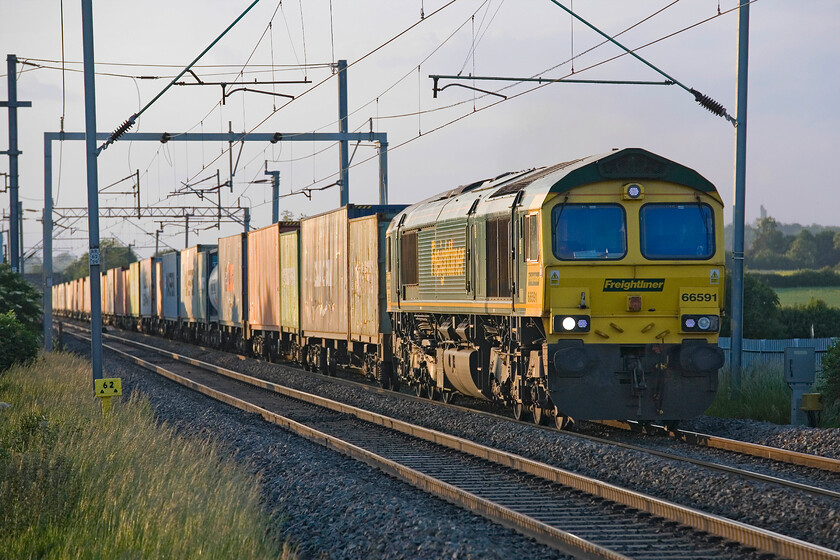 66591, 14.18 Trafford Park-Felixstowe (4L96), Milton Malsor SP740553 
 The gathering cloud from the east has turned an otherwise blue sky a strange hue as the sun sets on 2013's longest day. 66591 slogs up the steady gradient from Northampton towards Roade past Milton Malsor leading the 4L96 14.18 Trafford Park to Felixstowe Freightliner. The tail of the train is out of sight behind bushes that have grown up along the side of the line here in more recent years such is Network Rail's poor management of their linesides. 
 Keywords: 66591 14.18 Trafford Park-Felixstowe 4L96 Milton Malsor SP740553 Freightliner