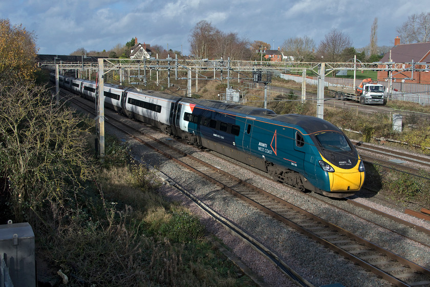 390128, VT 10.57 Preston-London Euston (1A16, 5E), site of Roade station 
 With further clearance having taken place for the installation of a missing link of palisade fencing below where I am standing, 390128 heads south past the site of Roade's former station with the 10.57 Preston to Euston. After a dull start to the day the sun has come out but it looks as if we are in for a shower given the dark and ominous sky behind! 
 Keywords: 390128 10.57 Preston-London Euston 1A16 site of Roade station Avanti West Coast Pendolino